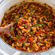 Goulash with macaroni, ground beef, and vegetables in a white pot.