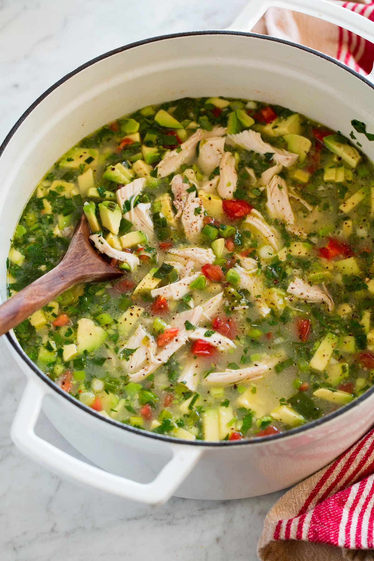 Chicken Avocado Soup White pot filled with chicken soup with avocado and tomatoes.