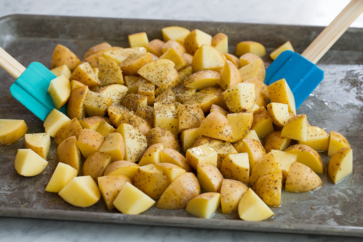 Lemon Roasted Potatoes Tossing potatoes with oil, lemon and seasonings using silicone spatulas. Potatoes are on a alluminum baking sheet.