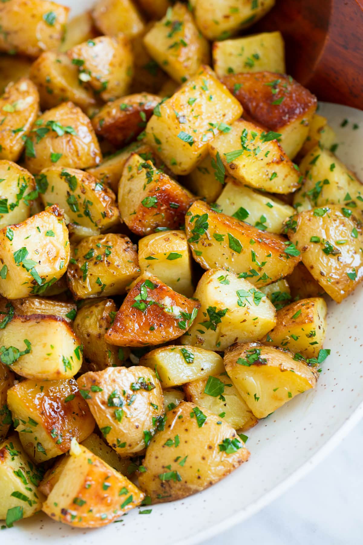 Lemon Roasted Potatoes Close up image of roasted potatoes with lemon and parsley in a white serving bowl.
