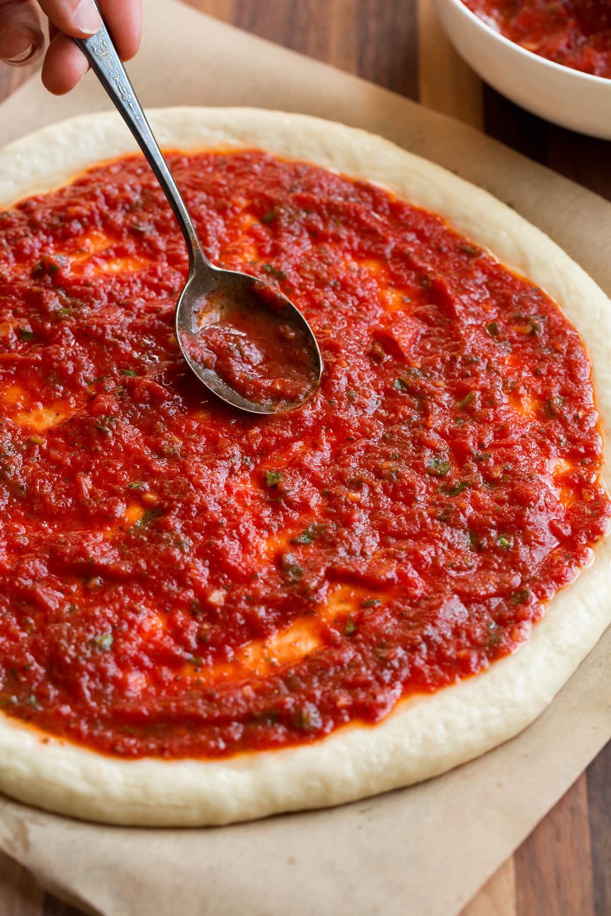 Homemade Pizza Sauce Spooning homemade pizza sauce over a round of pizza dough.