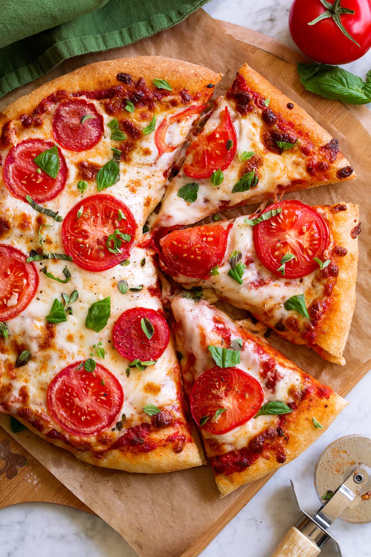 Homemade Pizza Sauce Pizza topped with red pizza sauce, mozzrella, tomatoes and herbs. It is cut into slices and sitting on parchment paper over a wooden pizza peel.