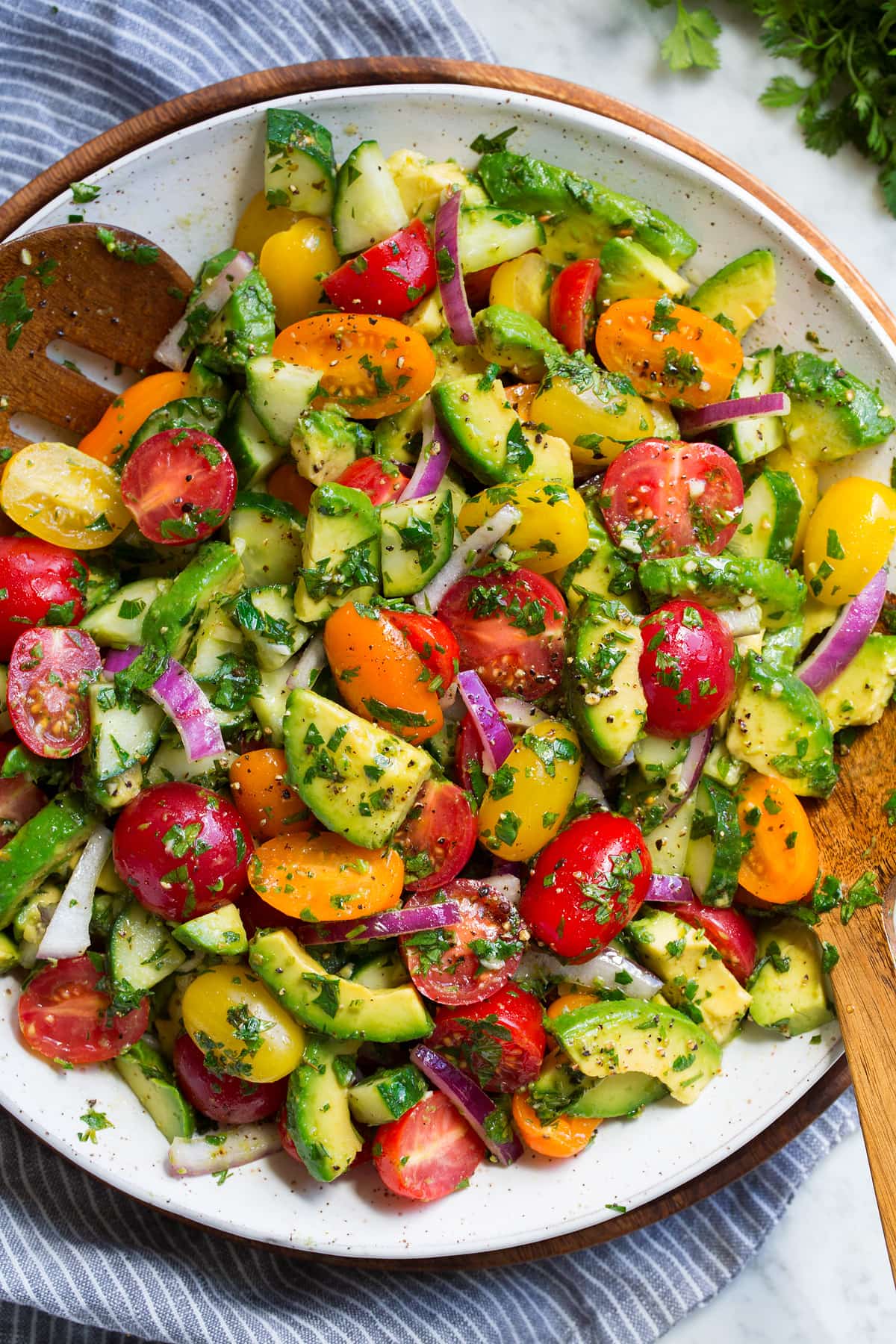 Avocado Salad Avocado salad with fresh avocados, grape tomatoes, red onion, cucumbers and fresh herbs in a serving bowl.