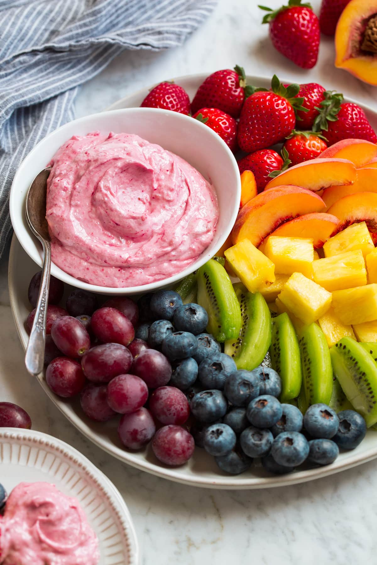 Easy Cream Cheese Fruit Dip Cream cheese fruit dip in a white bowl served on a platter with fresh strawberries, peaches, pineapple, kiwi, blueberries and grapes.