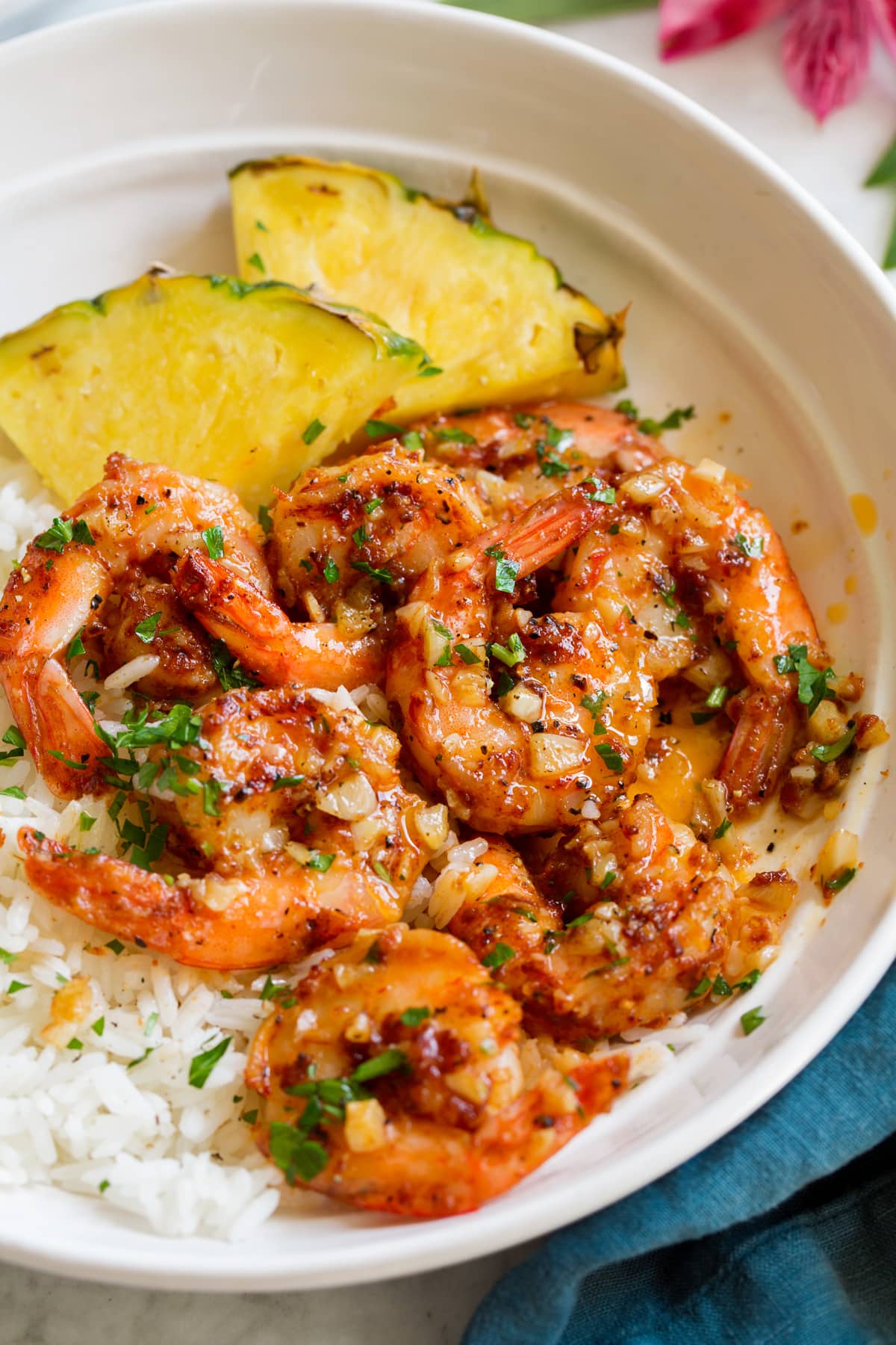 Hawaiian Garlic Shrimp Close up image of Hawaiian garlic shrimp served over white rice with slices of fresh pineapple.