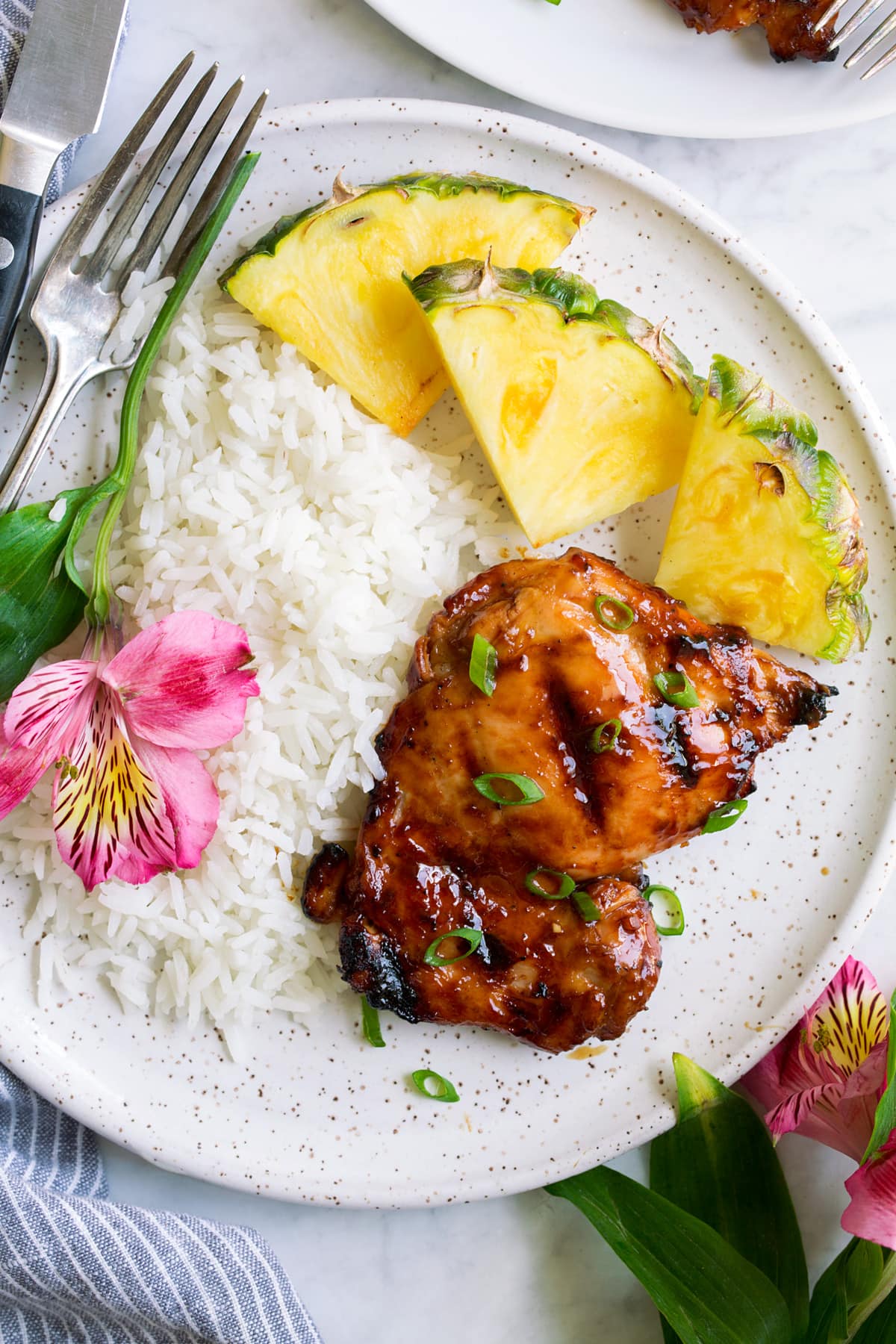 Huli Huli Chicken Plate with 1 huli huli chicken piece, pineapple, rice and a fresh flower. Shown overhead.