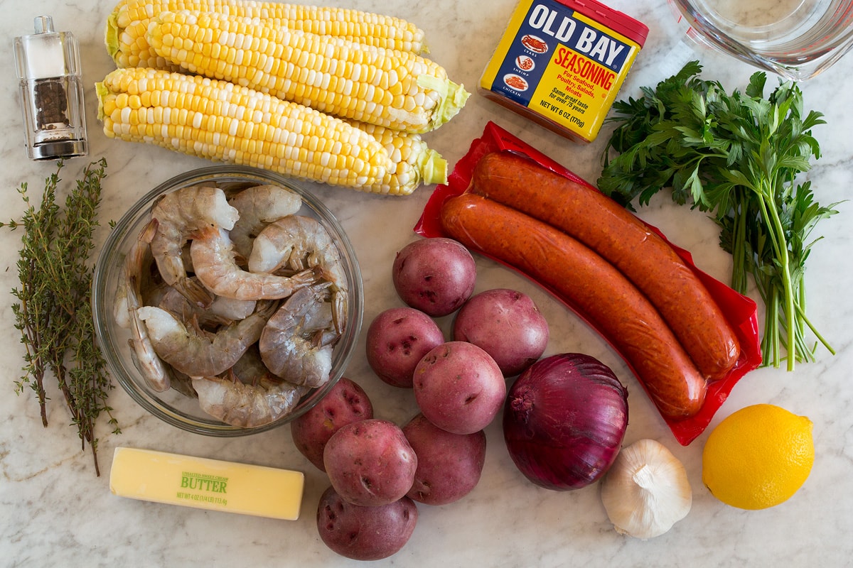 Shrimp Boil Image of ingredients used to make shrimp boil. Includes shrimp, corn on the cob, andouille sausage, red potatoes, onion, butter, lemon, parsley, thyme, garlic, salt and pepper and water.