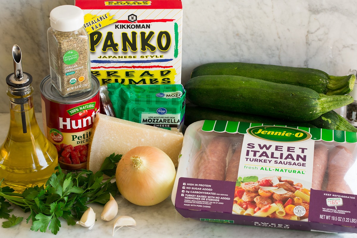 Zucchini Boats Image of ingredients used to make zucchini boats. Shows sausage, zucchini, onion, parmesan, parsley, garlic, mozzarella, tomatoes, Italian seasoning, panko bread crunbs and olive oil.