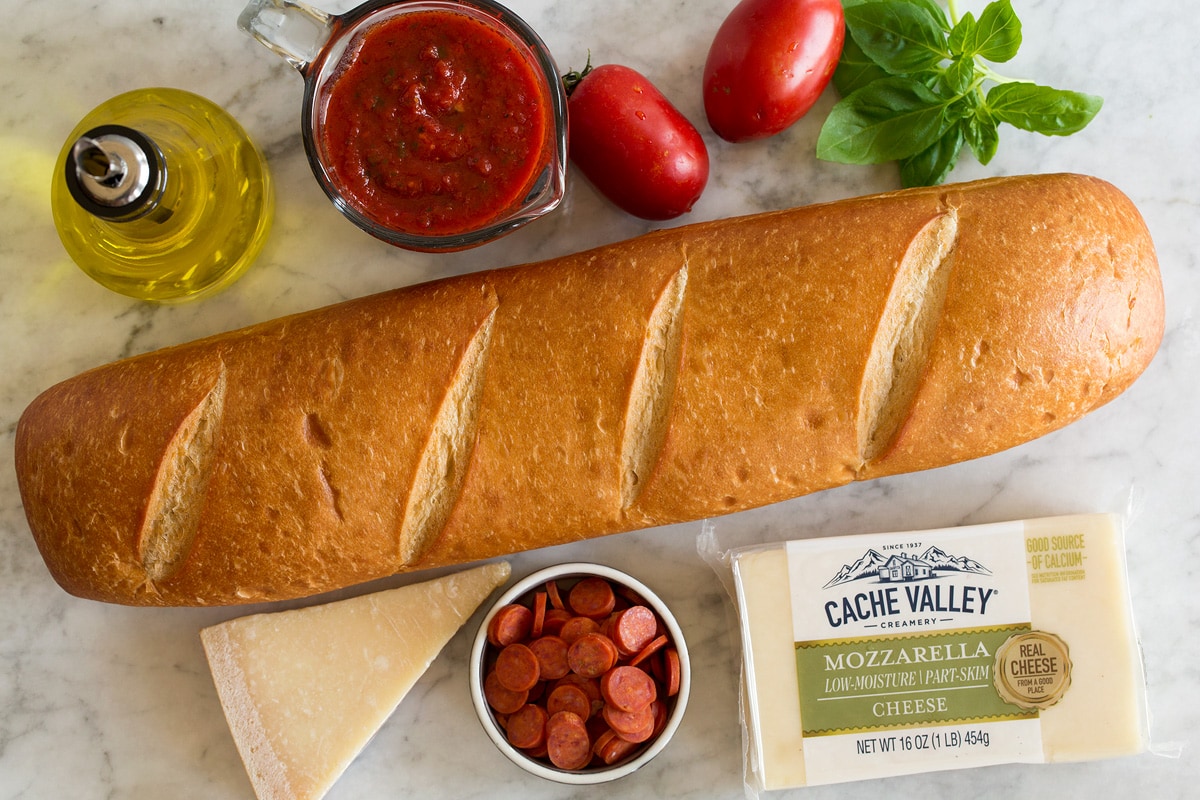 French Bread Pizza Image showing ingredients used to make French bread pizza. Includes French bread, cheeses, basil, pizza sauce, olive oil, pepperoni, tomatoes and basil.