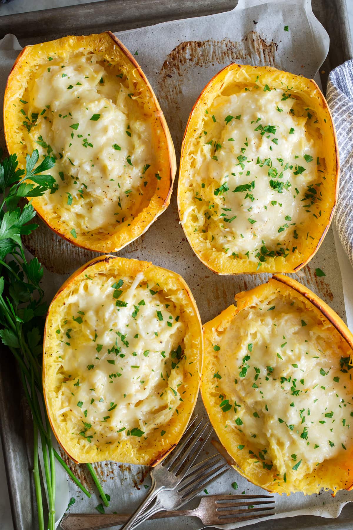 Cheesy Spaghetti Squash Overhead image of four spaghetti squash filled with cheese, they are resting on a parchment paper lined baking sheet.