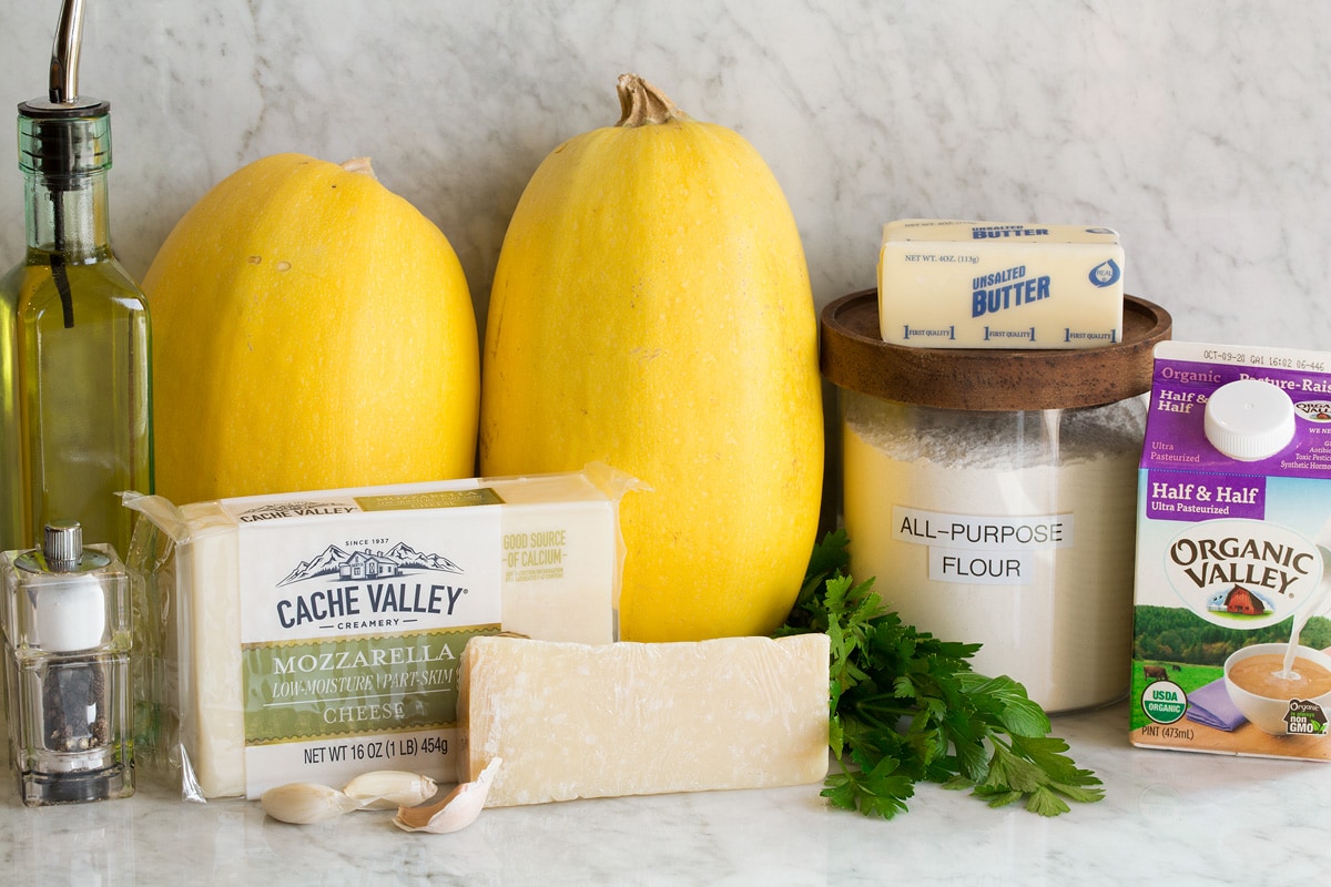 Cheesy Spaghetti Squash Image of ingredients used to make cheesy spaghetti squash shown. Includes spaghetti squashes, mozzarella, parmesan, half and half, flour, butter, olive oil, garlic, parsley, salt and pepper.