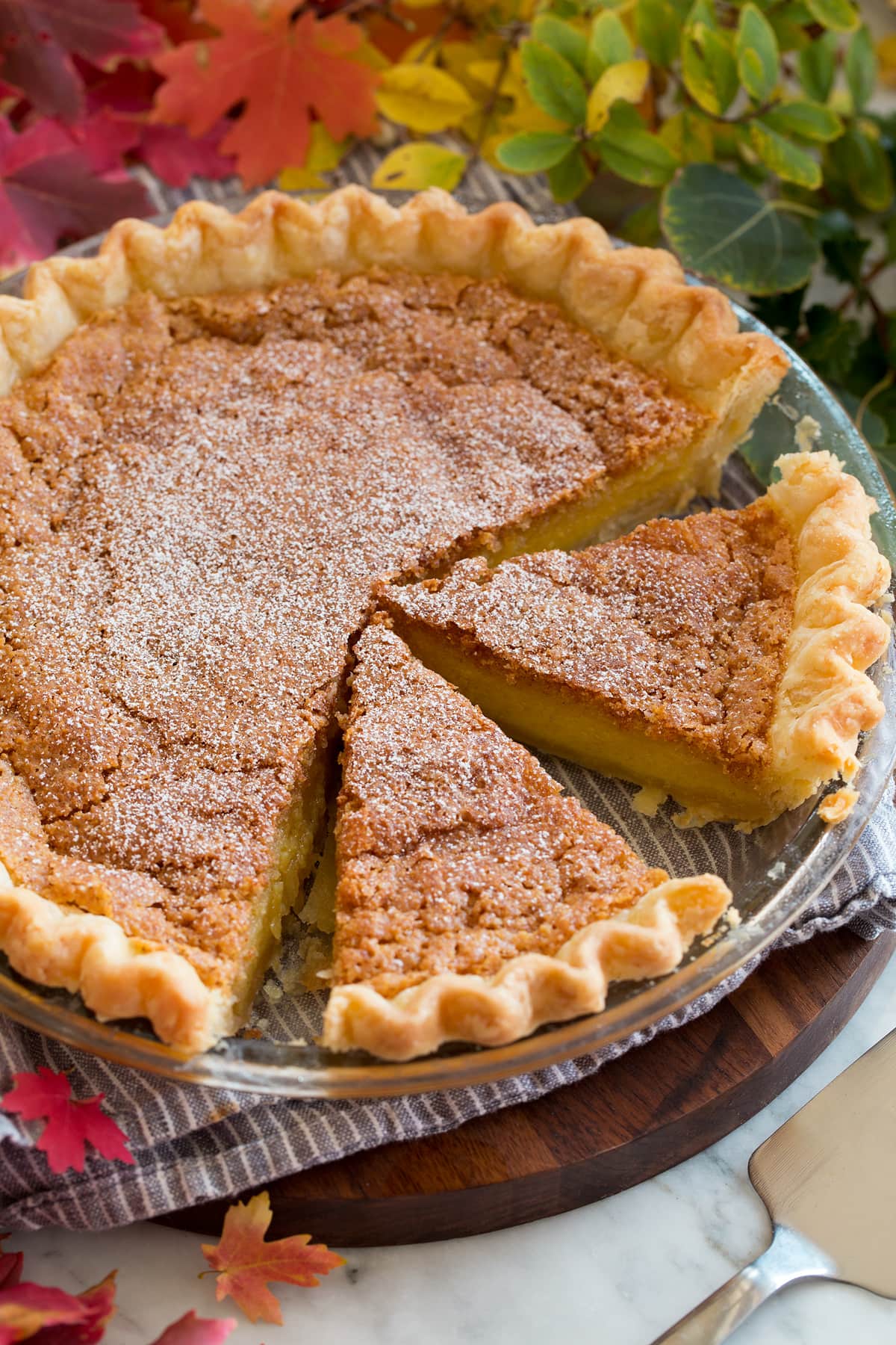 Chess Pie Image of chess pie cut into slices. Pie is shown in a glass baking dish set over a grey cloth on a wooden serving tray.
