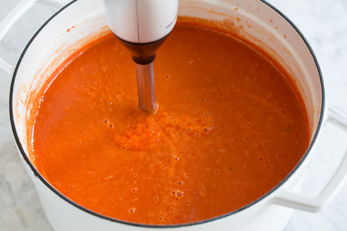 Homemade Tomato Soup Image of tomato soup being blended with an immersion blender in a pot.