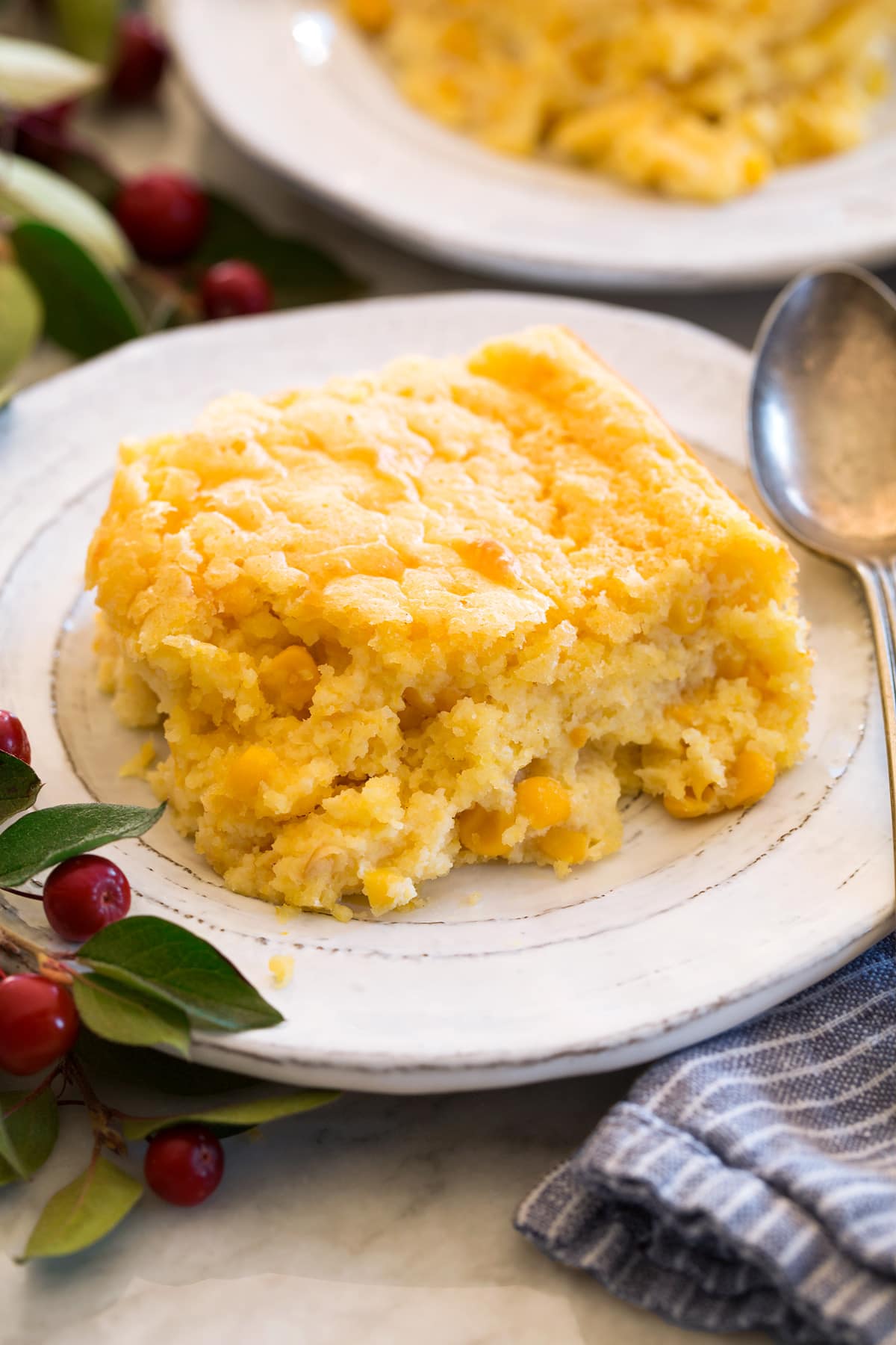 Corn Casserole Single serving of corn casserole shown on a white plate with a spoon to the side.