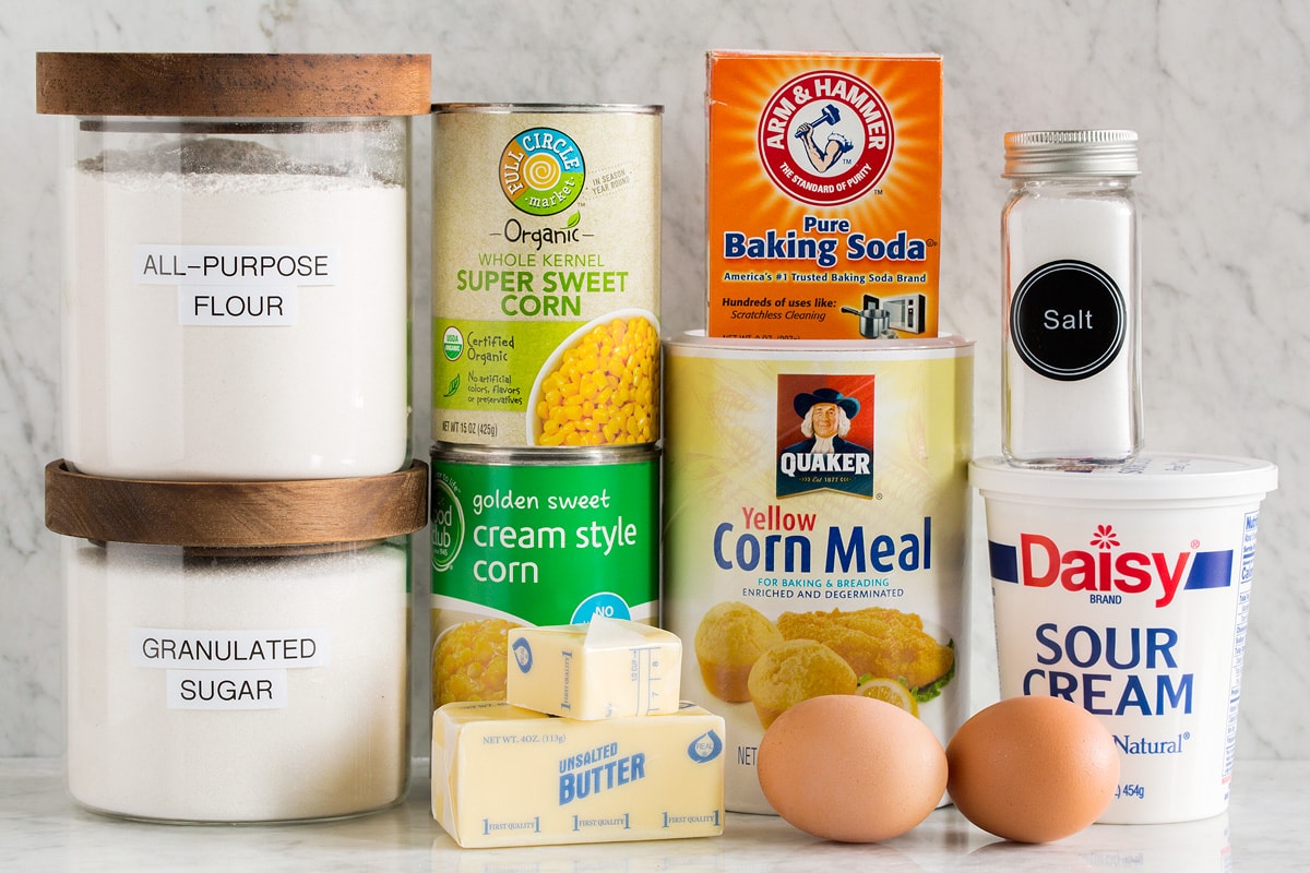 Corn Casserole Image of ingredients needed to make corn casserole from scratch. Includes canned corn and creamed corn, flour, sugar, baking soda, sour cream, corn meal, salt, eggs and butter.