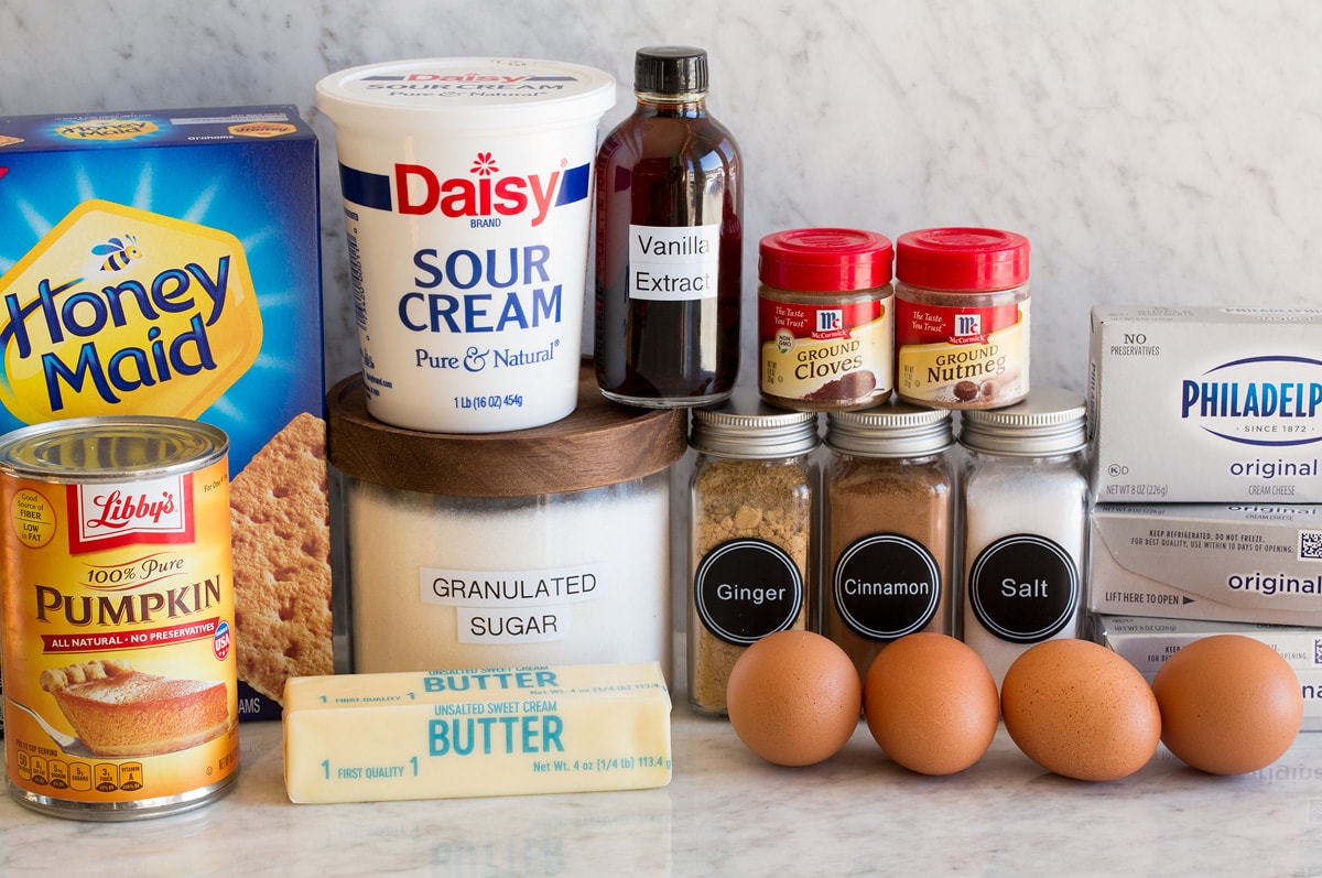 Pumpkin Cheesecake Image of ingredients needed to make pumpkin cheesecake. Includes graham crackers, sugar, butter, cream cheese, eggs, pumpkin, spices, sour cream and vanilla.