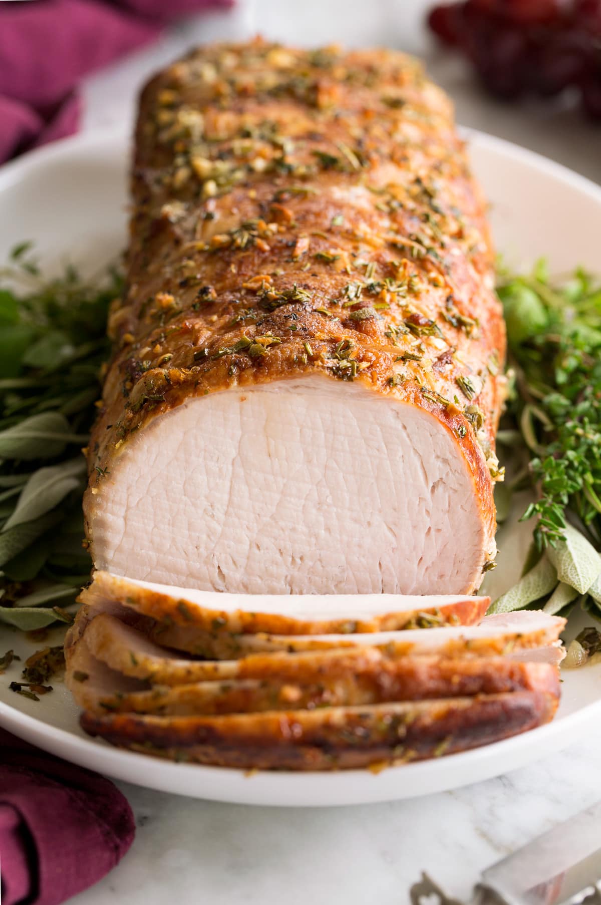 Pork Loin Pork Loin Roast served on a white platter with fresh herbs. Pork is shown sliced at the forefront.