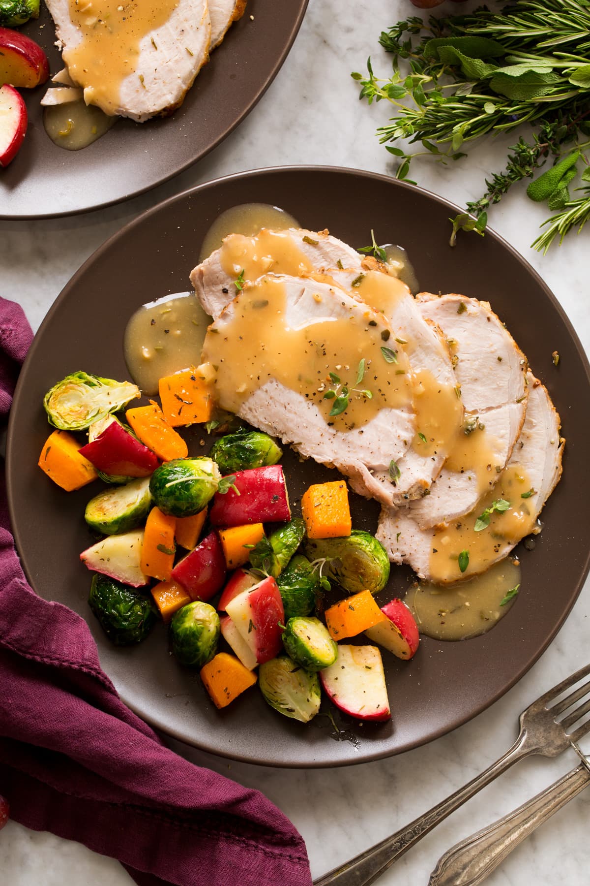 Pork Loin Roast Pork loin shown cooked and sliced with gravy atop. Shown on a brown plate with a side of roasted vegetables and apples.