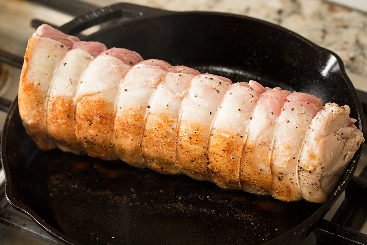 Pork Loin Roast Pork loin being seared and browned in a cast iron skillet on the stovetop.