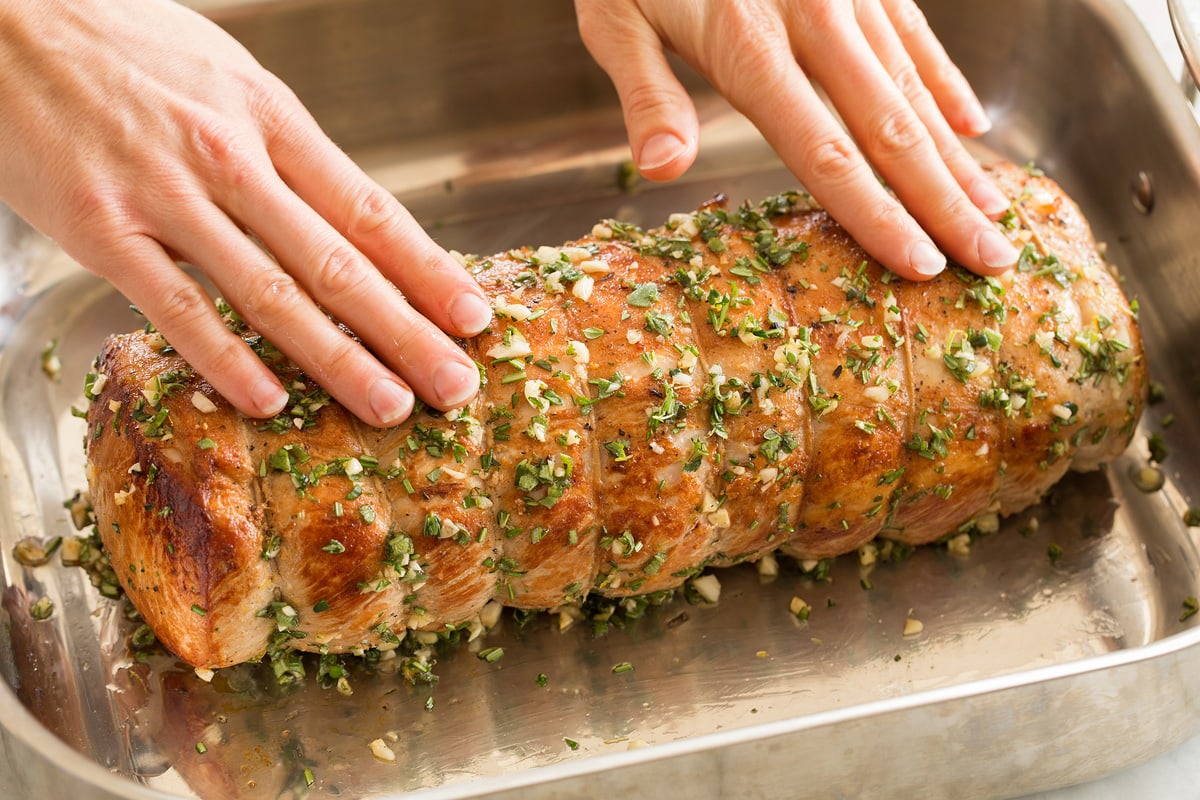 Pork Loin Roast Rubbing herbs and garlic over pork loin in a roasting pan.