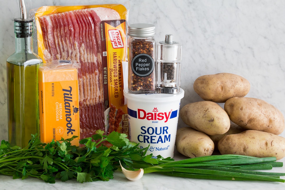 Potato Skins Photo of ingredients used to make potato skins. Includes russet potatoes, bacon, olive oil, cheddar cheese, sour cream, salt, pepper, red pepper flakes, parsley, green onions and garlic.