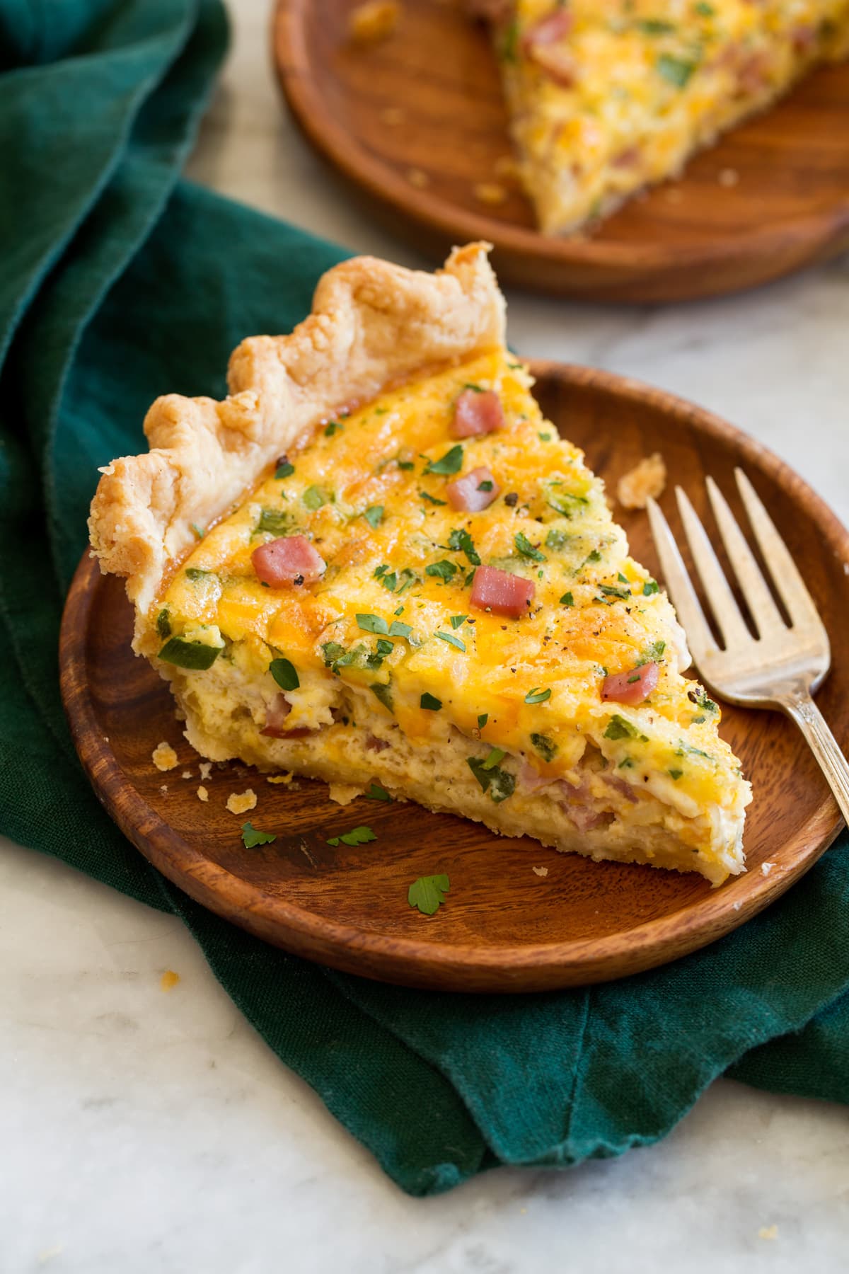Quiche Slice of ham and cheese quiche on a wooden plate set over a green napkin.