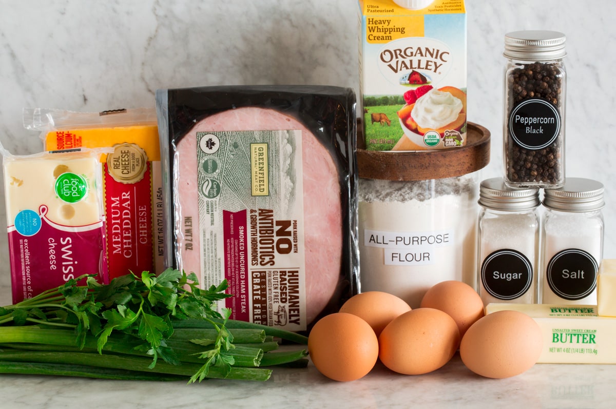 Quiche Photo of ingredients used to make a homemade quiche and crust. Includes flour, butter, salt, sugar, pepper, eggs, parsley, green onions, ham, cheddar and Swiss cheese.