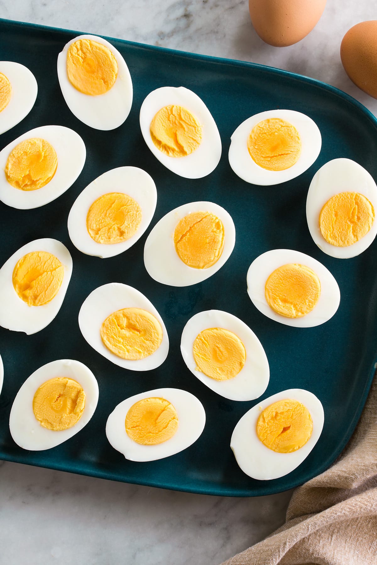 Steamed Eggs Photo: 15 steamed egg havles in half shown on a blue rectangular platter on a marble surface.