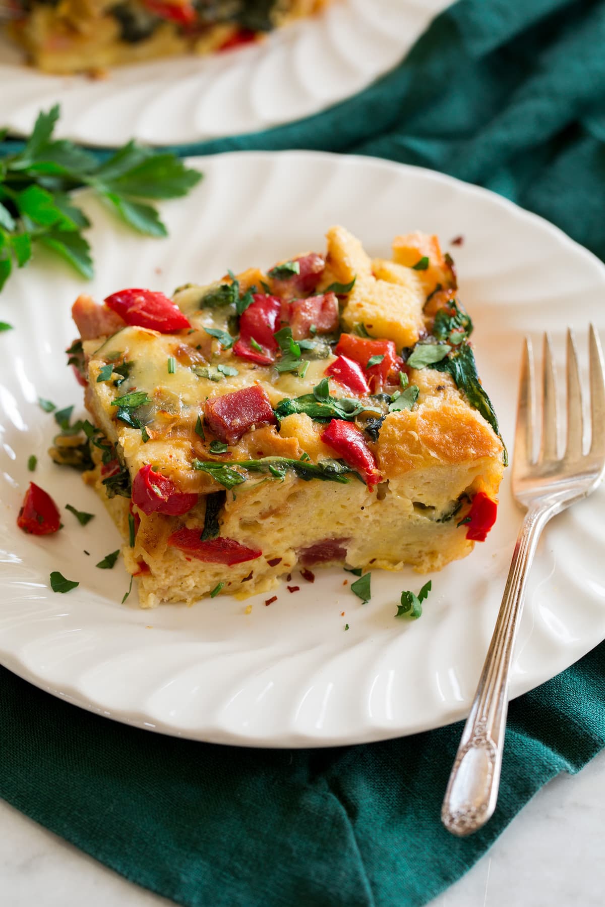Strata Photo of slice of strata on a single serving plate with a fork to the side. Plate is set over a green cloth.
