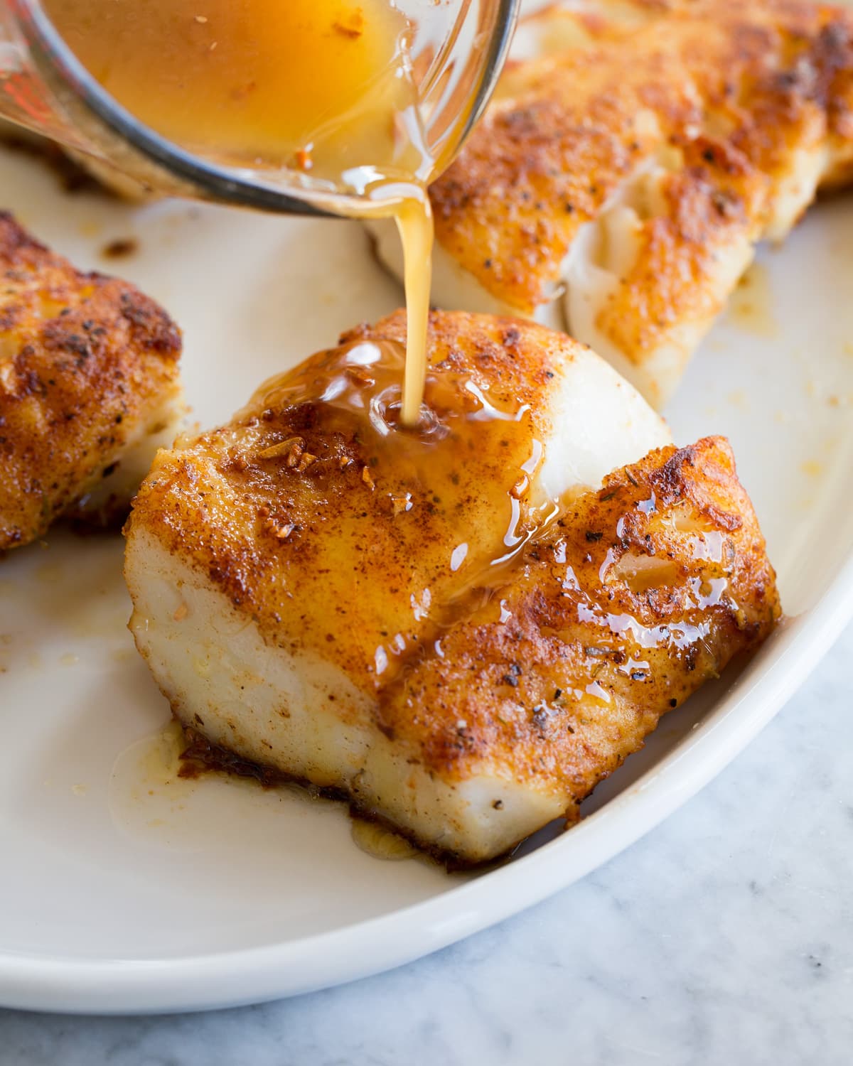 Lemon Butter Cod Sauce being poured over cooked white fish fillet on a platter.