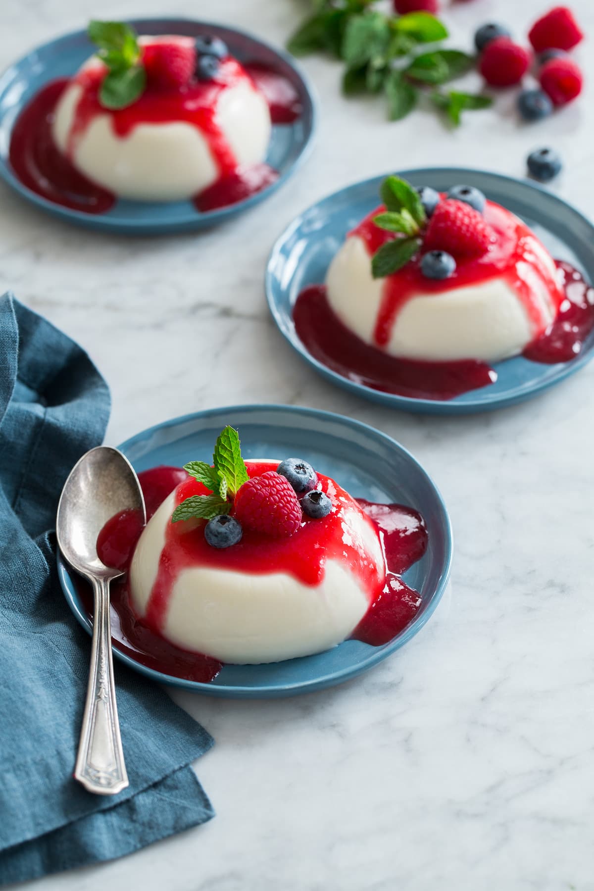 Panna Cotta Photo: Three servings of homemade panna cotta shown on dessert plates on a white marble surface.