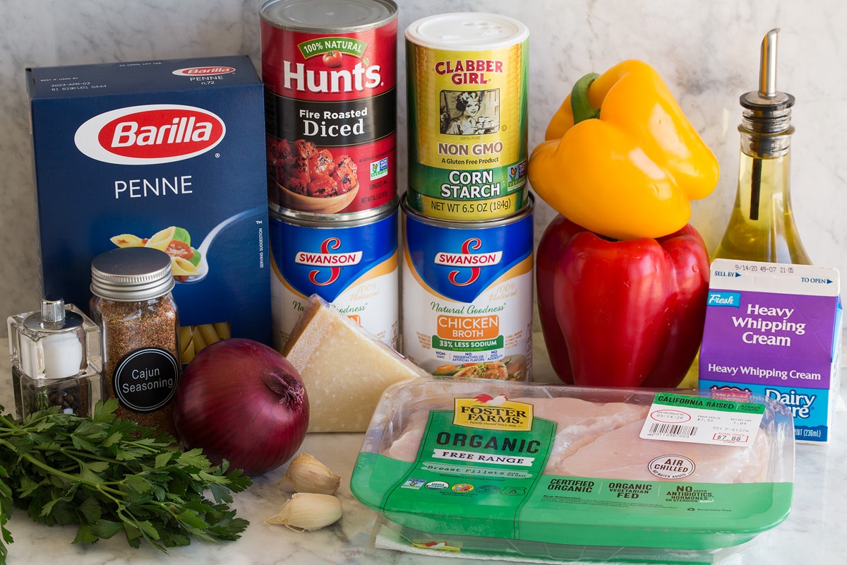 One Pot Cajun Chicken Pasta Photo of ingredients. Includes penne pasta, chicken, cream, bell peppers, olive oil, cornstarch, chicken broth, parmesan, tomatoes, red onion, garlic, parsley, salt and pepper.