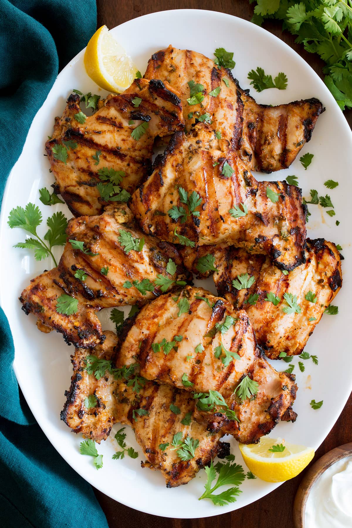 Greek Yogurt Marinated Grilled Chicken Yogurt Marinated Grilled Chicken shown from above on a white oval platter on a wooden table with a turquoise cloth to the side.