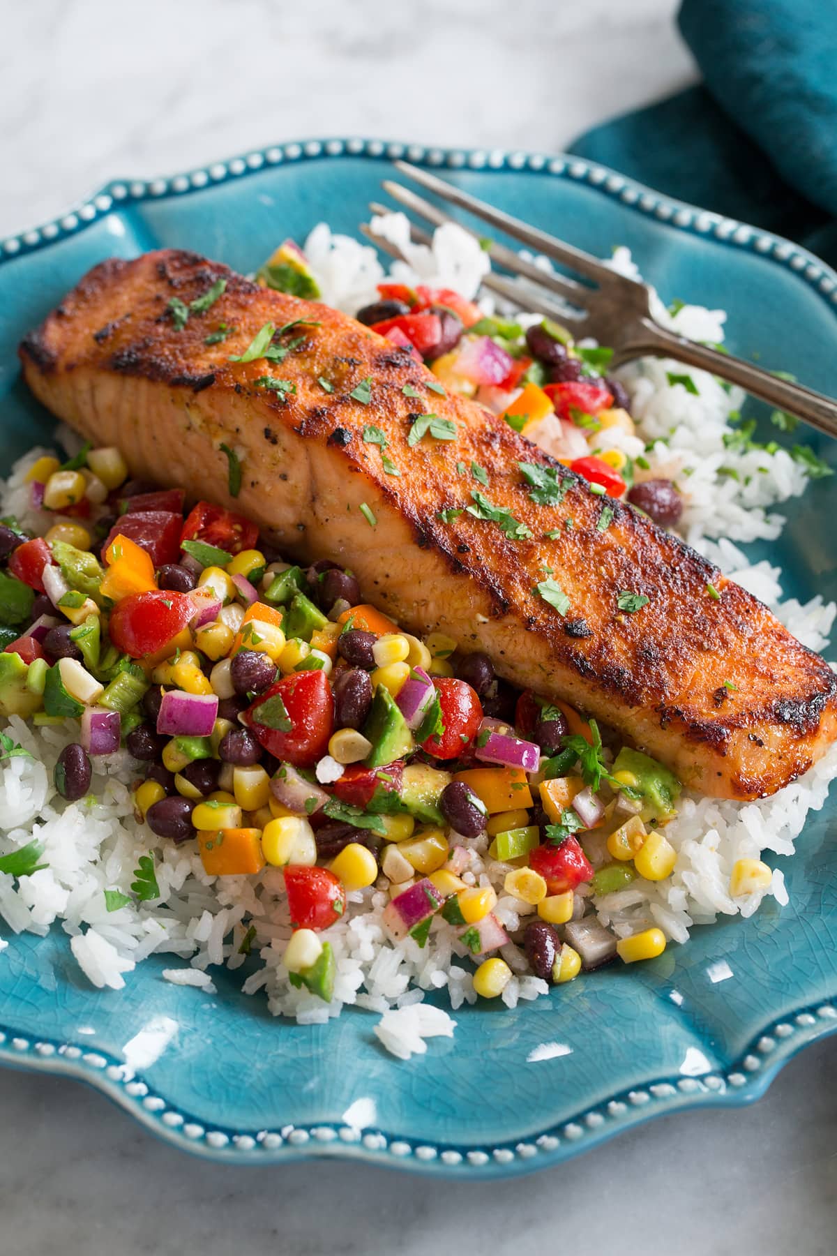 Broiled Salmon Broiled salmon shown served over a black bean corn salsa and rice on a blue plate.