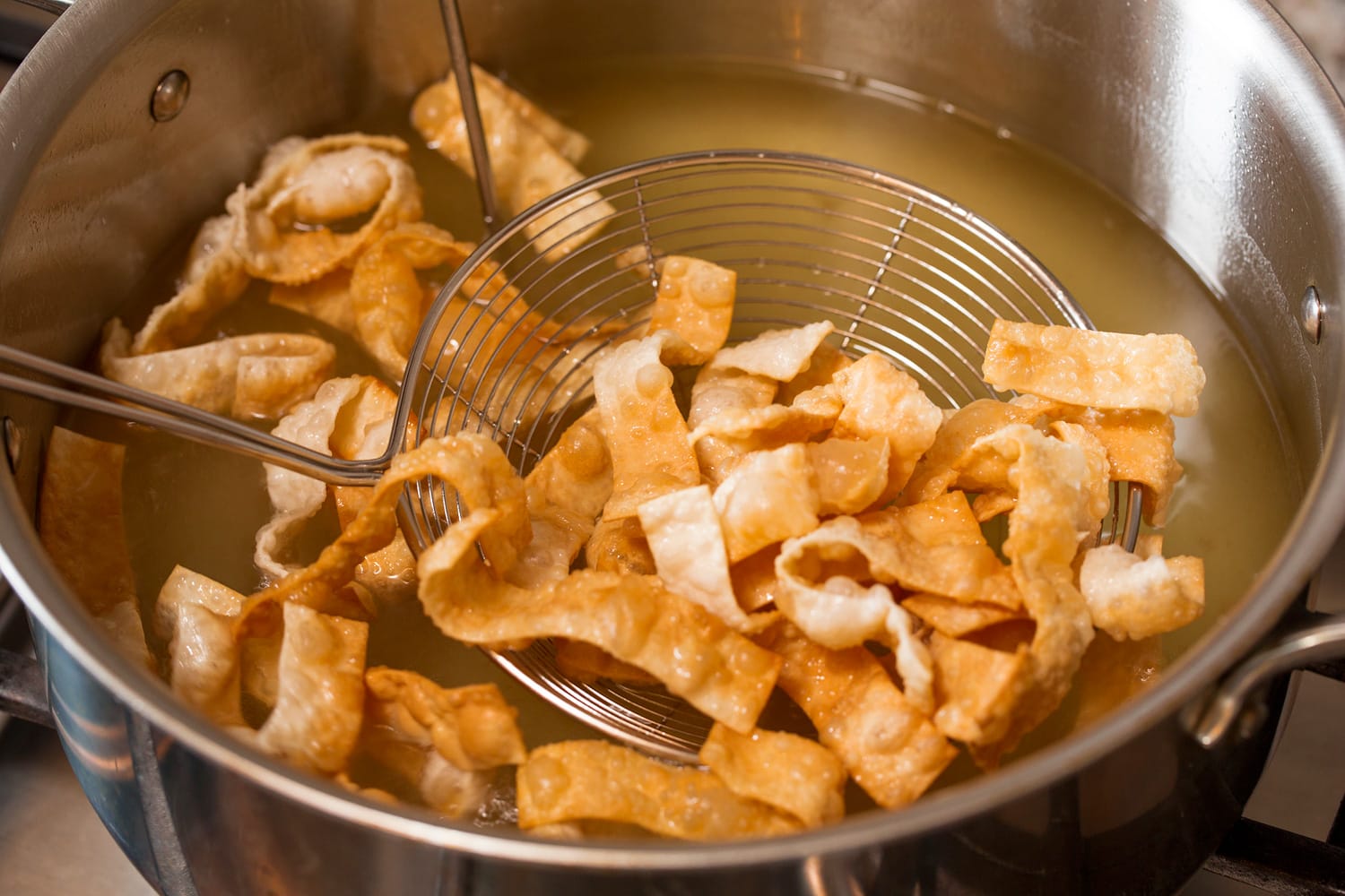 Fried Wonton Strips Golden brown fried wonton strips being removed from oil.