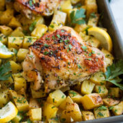 Close up photo of lemon chicken thighs and potatoes on a baking sheet.