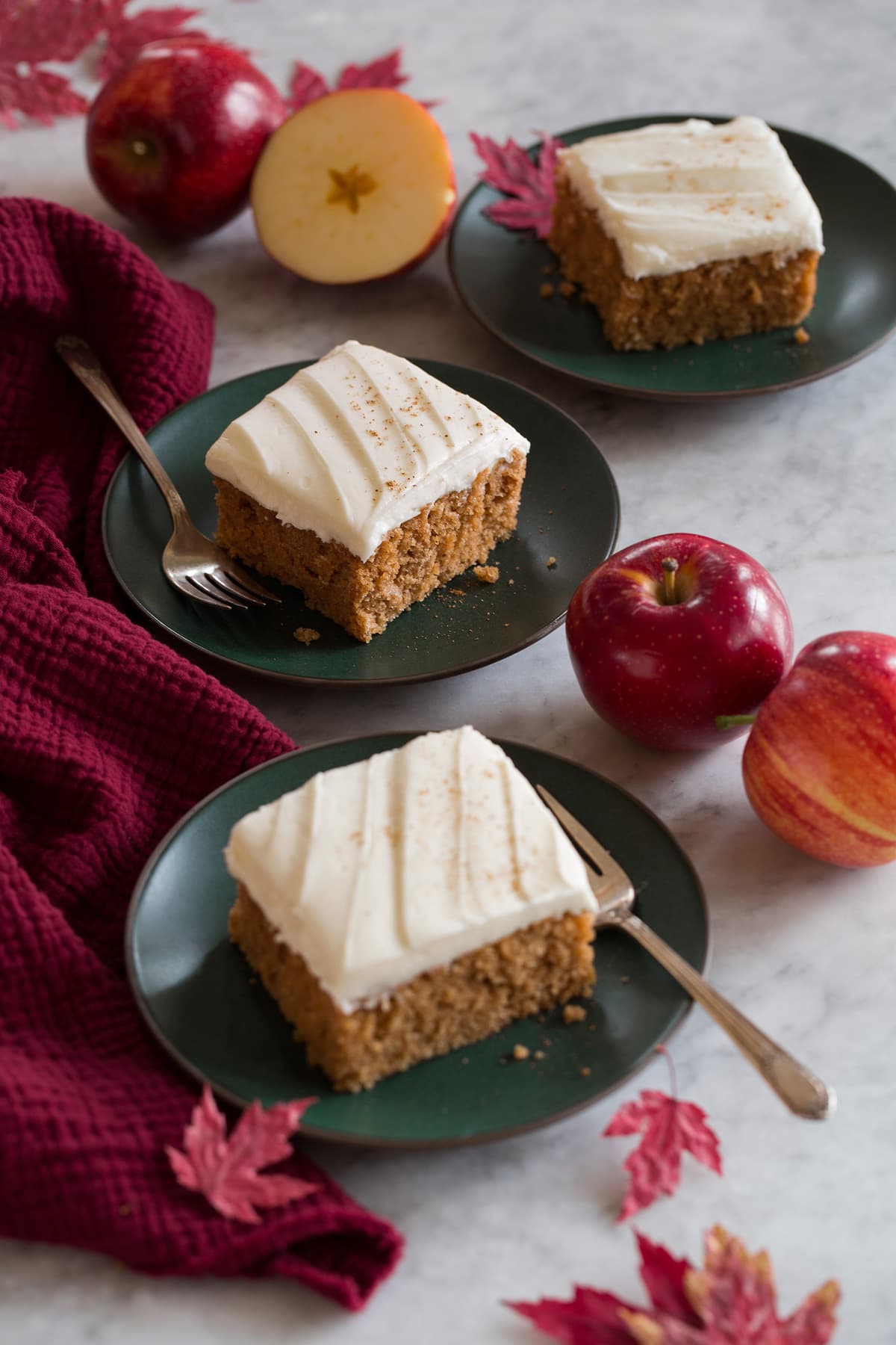 Applesauce Cake Three slices of applesauce cake shown on green dessert plates with apples, autumn leaves, and a red cloth to the sides.