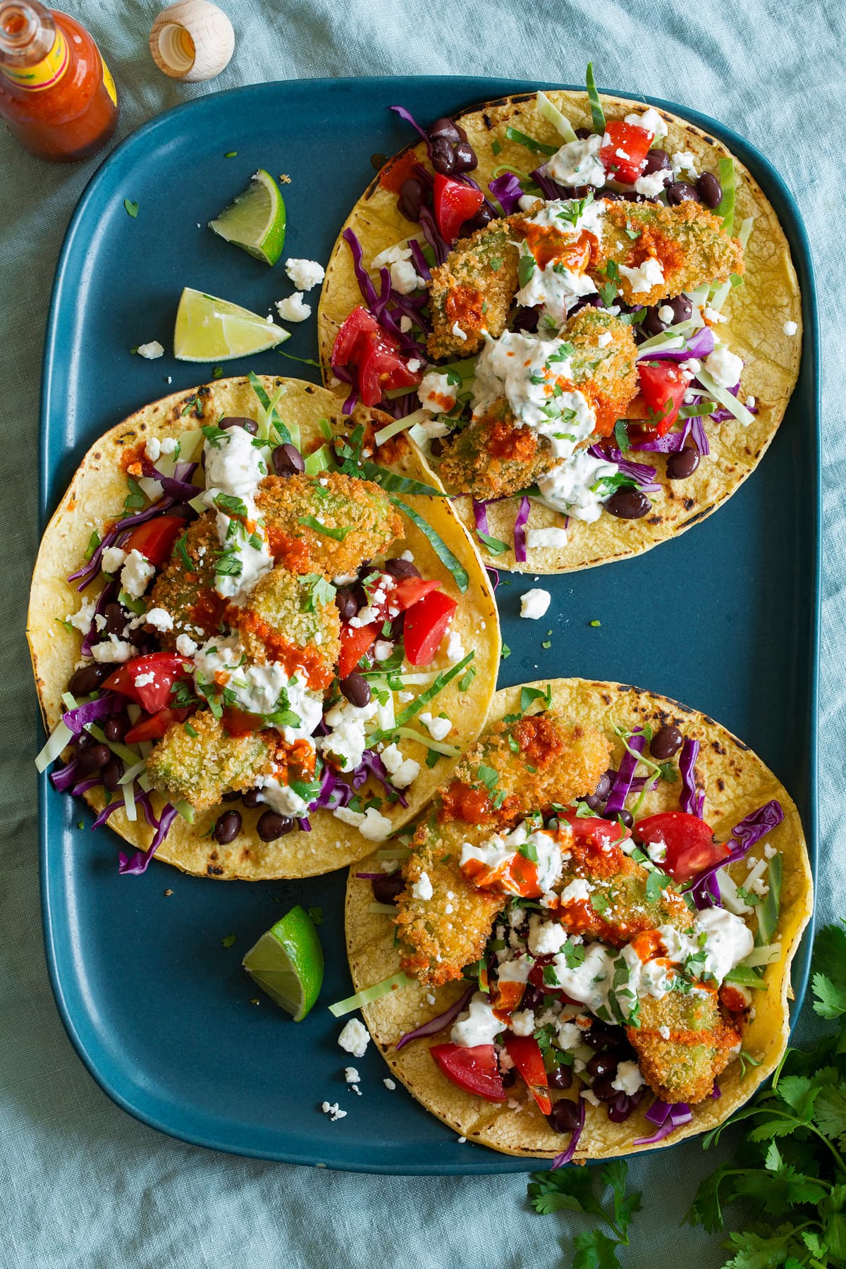 Avocado Tacos Three avocado tacos shown on a blue platter from above. Tacos are made with avocado fries, tomatoes, cabbage, cilantro sauce, cheese and black beans.