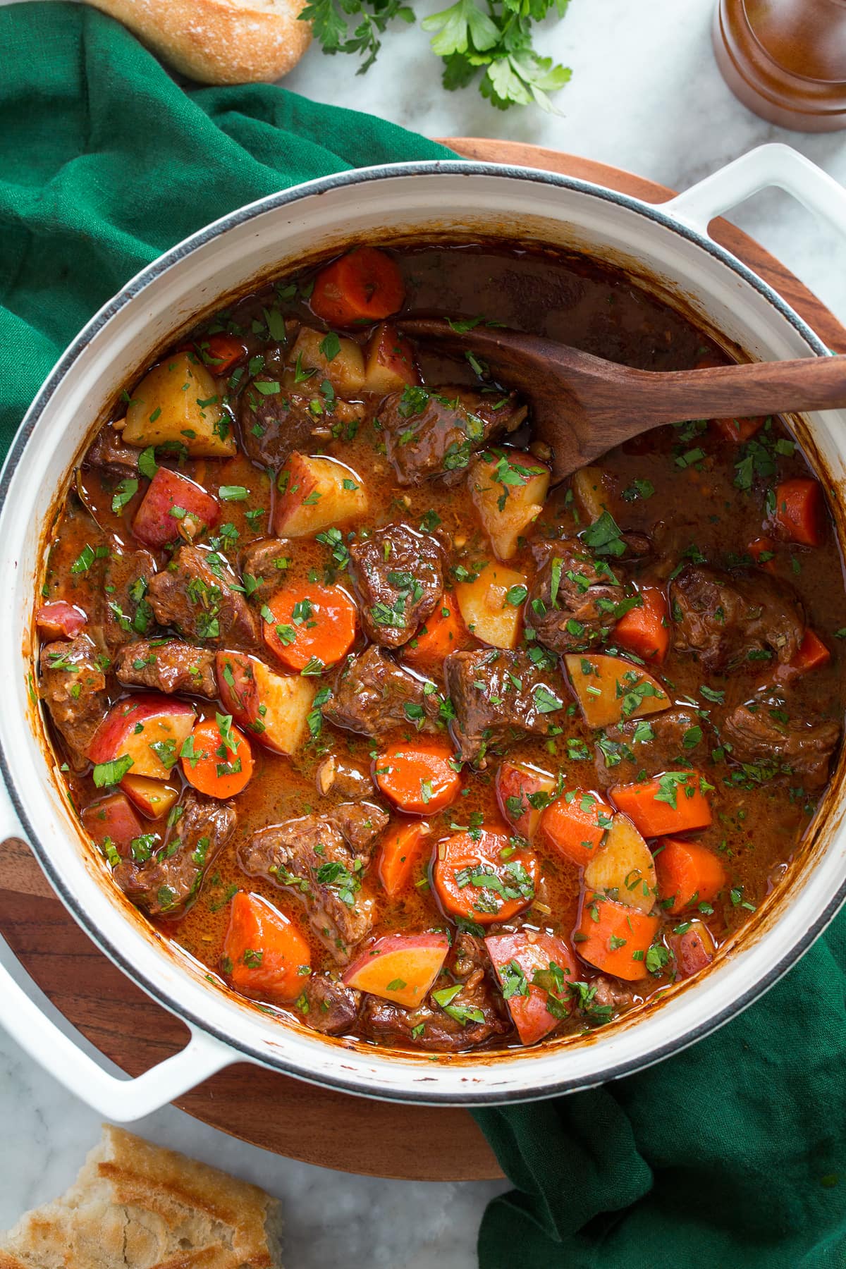 Beef Stew Beef stew shown in a large white pot from overhead. It is resting on a green cloth over a wooden platter.