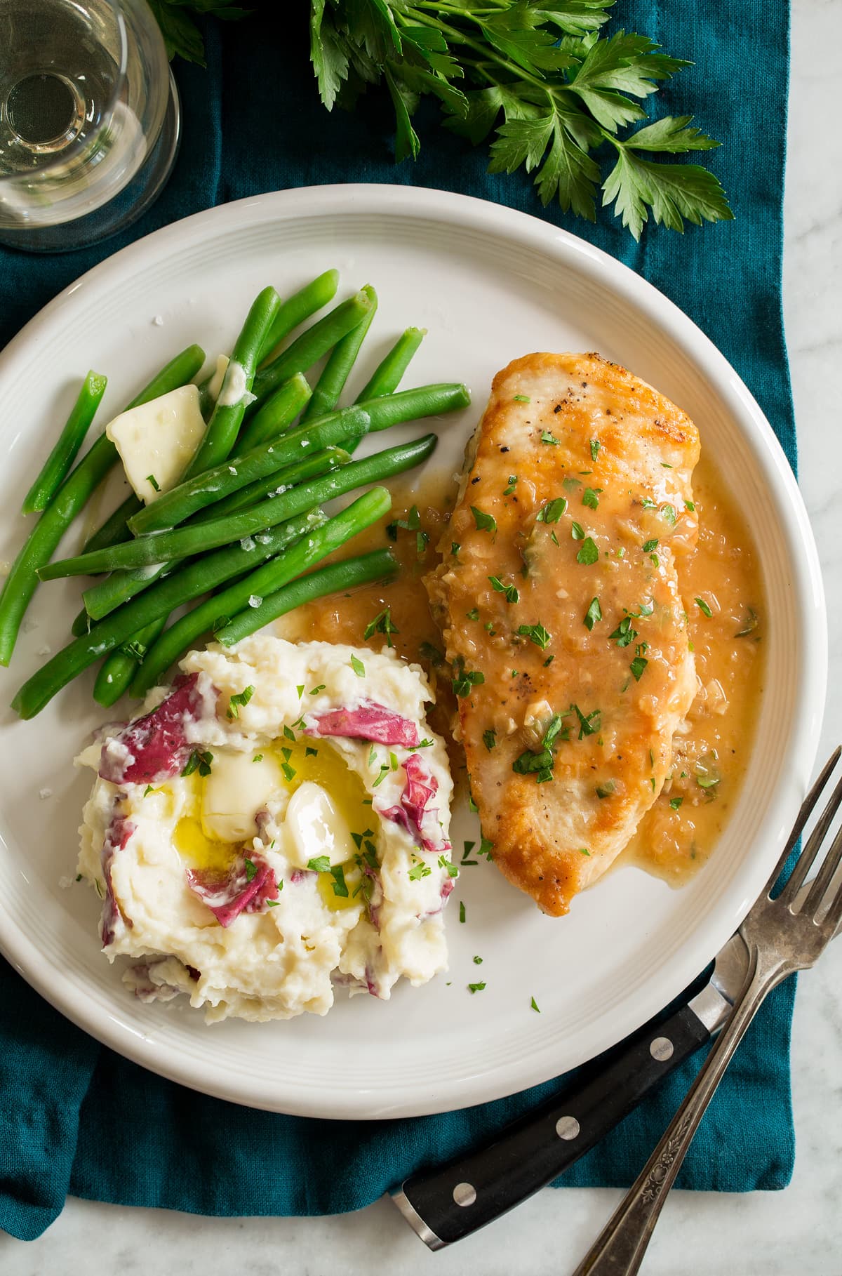 Chicken in White Wine Sauce Chicken in white wine sauce shown served with green beans and buttered mashed potatoes on a white dinner plate.