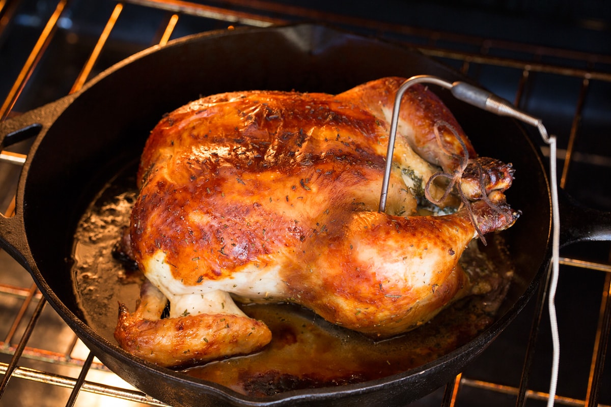Buttermilk Roast Chicken Photo of a browned whole chicken roasting in the oven with a food thermometer inserted into the thigh.