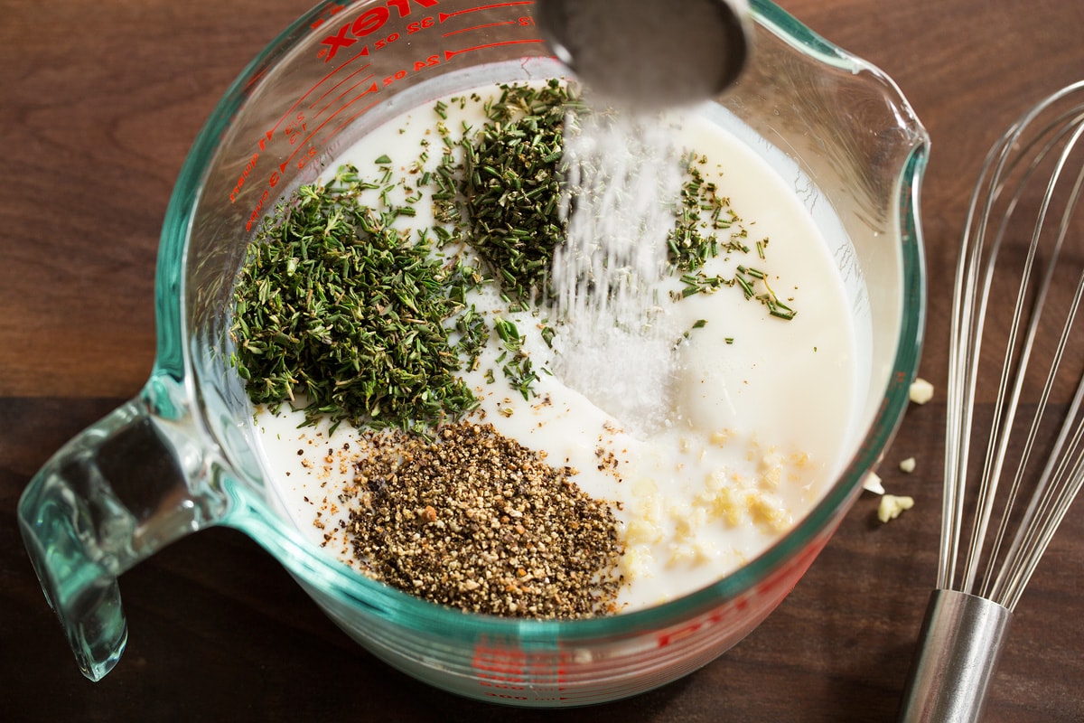 Buttermilk Roast Chicken Buttermilk, salt, herbs, garlic and pepper shown before mixing in a glass measuring cup.