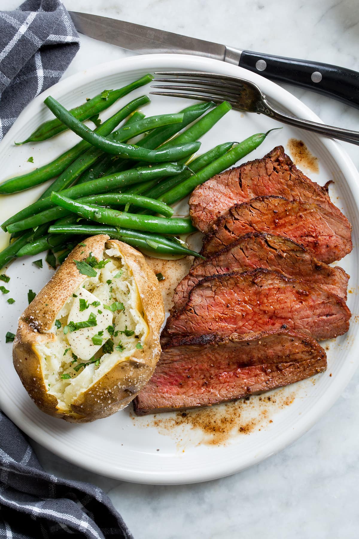 Roasted Tri Tip Roasted tri tip on a white plate shown with serving suggestion of baked potato and steamed green beans.