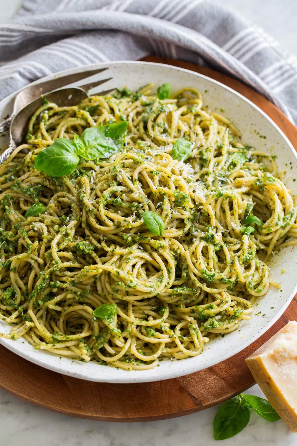 Pesto Pasta Homemade pesto tossed with spaghetti pasta in a large white serving bowl set over a wooden platter.
