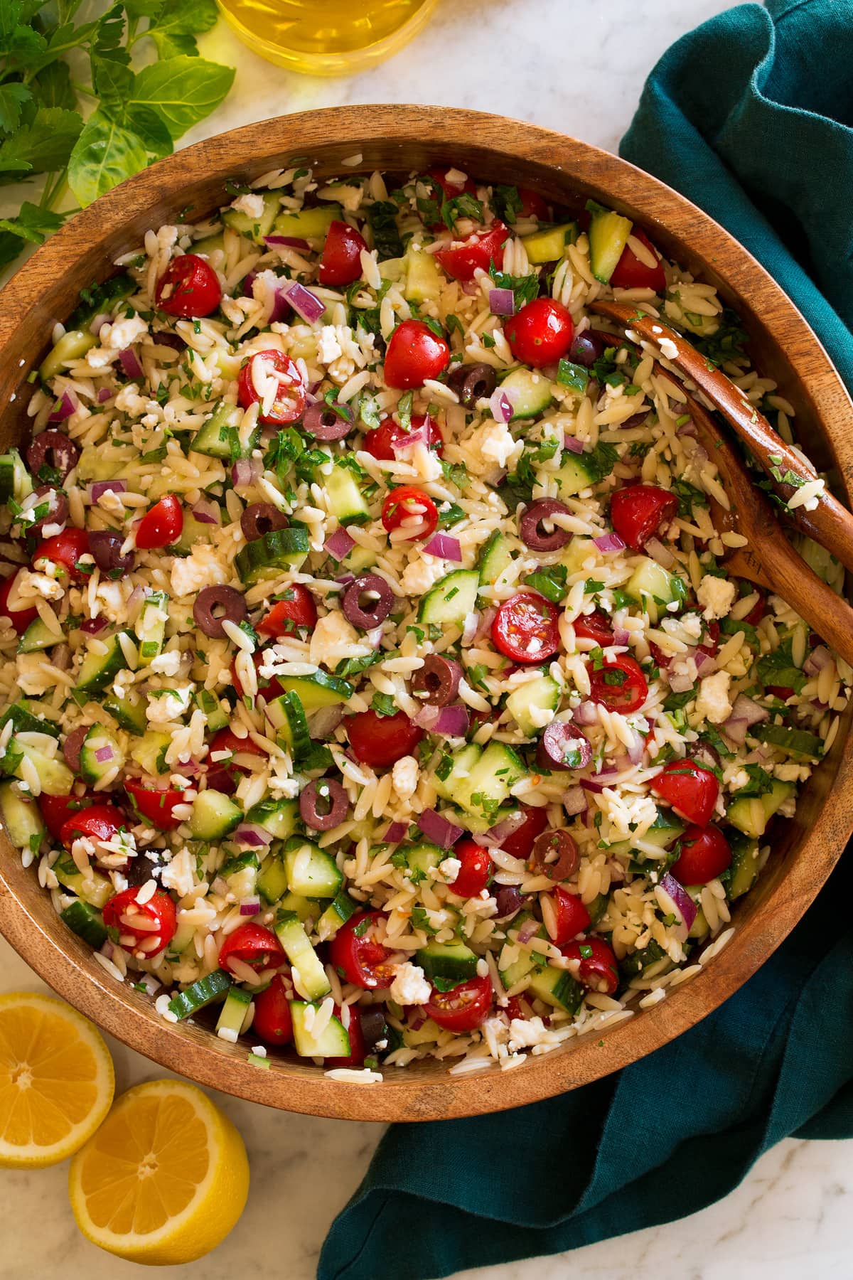 Greek Orzo Pasta Salad Orzo pasta salad in a large wooden bowl on a marble surface.