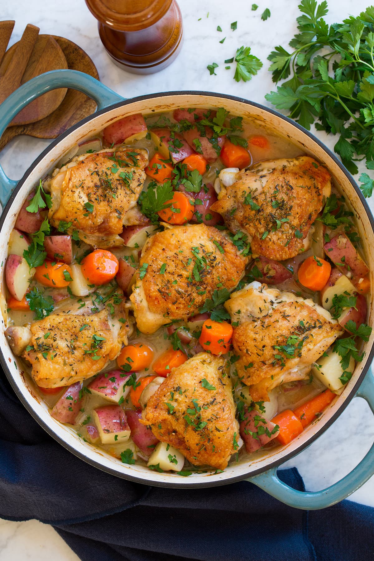 Braised Chicken and Vegetables Braised chicken thighs with bones and skin in a braiser pot with carrots and potatoes.