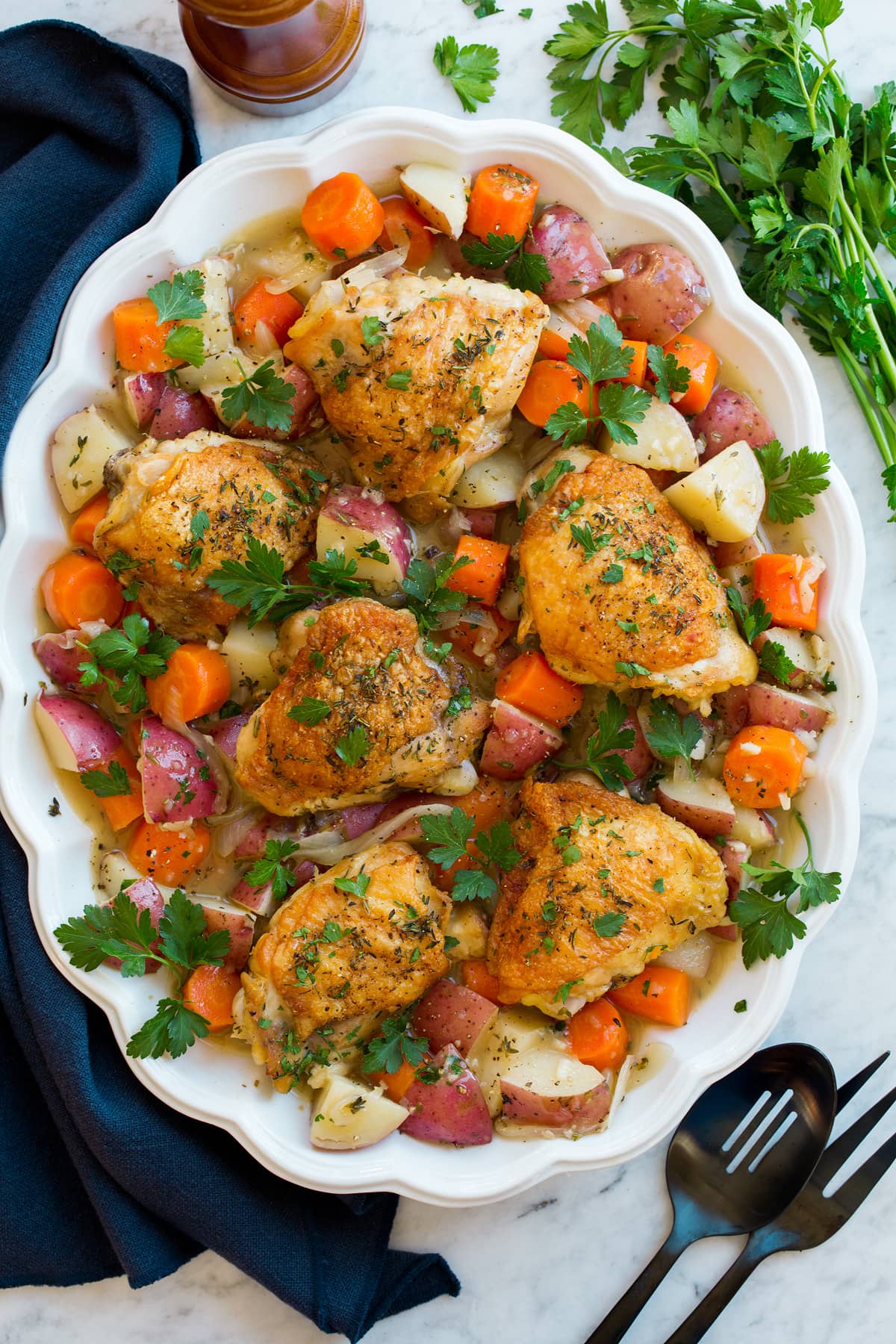 Braised Chicken Thighs and Vegetables Braised chicken and vegetables on a white oval platter on a marble surface..