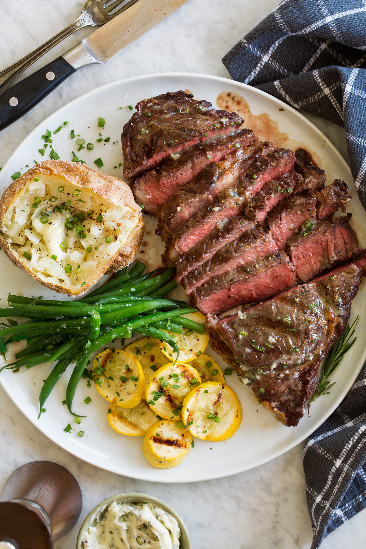 Grilled Steak Grilled steak shown sliced on a serving plate with a side or grilled squash, green beans and a baked potato.
