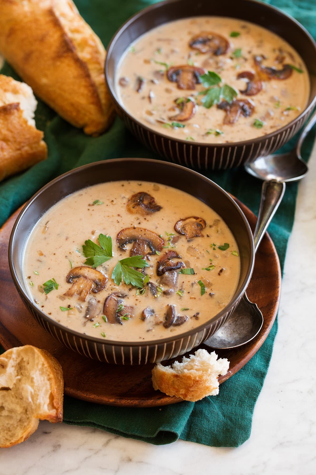 Cream of Mushroom Soup Two servings of mushroom soup in brown bowls sitting on a green cloth on a marble surface.