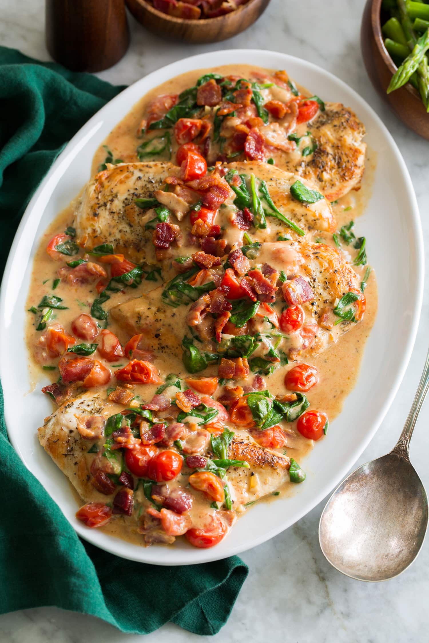BLT Chicken Creamy bacon tomato spinach chicken served on a white oval platter with a green cloth to the side.